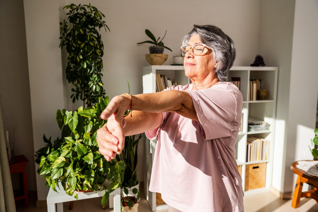 Older woman stretching her arm and wrist in a sunlit room