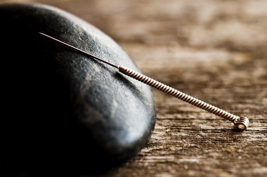Thin acupuncture needle being placed into skin during a session